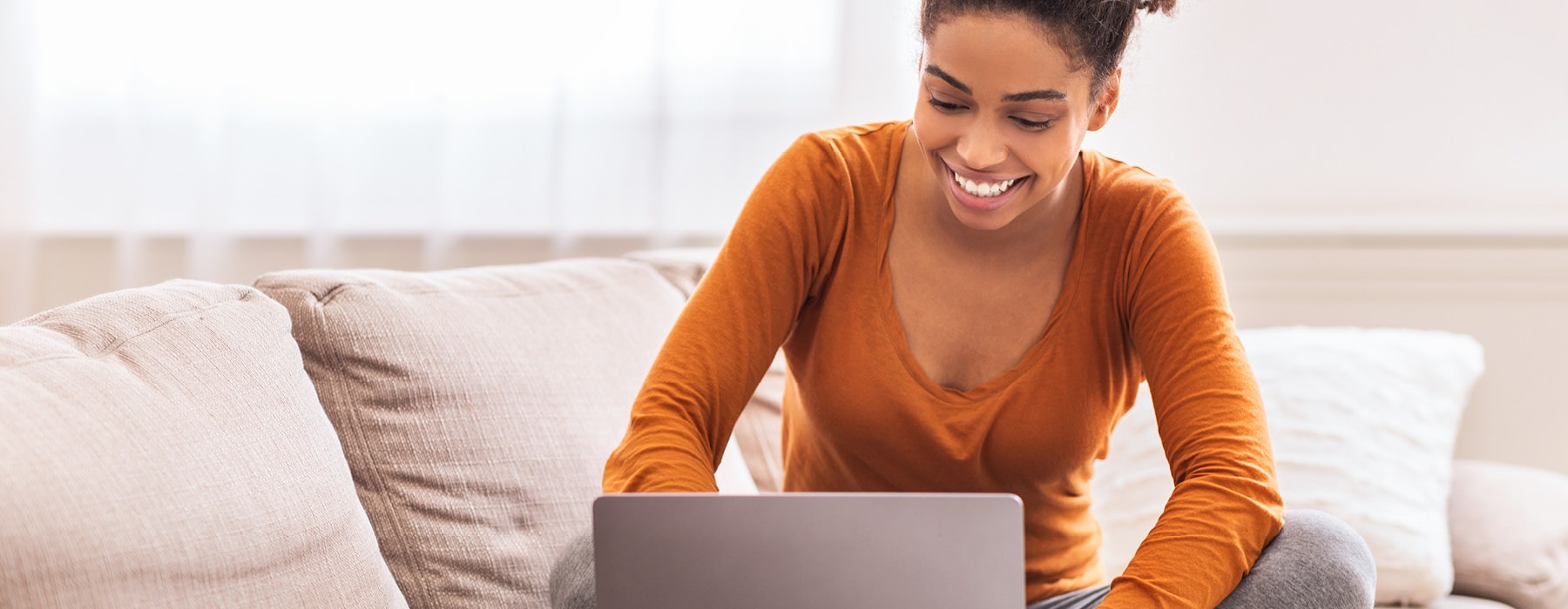 smiling woman sits on her couch and works on her laptop
